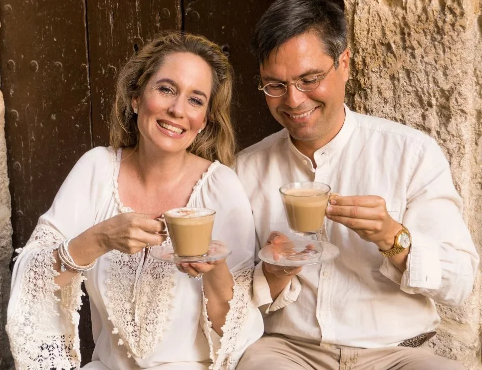 Suzanne und Dr. Ludwig Jacob mit zwei Tassen Chi-Cafe vor einer alten Holztür